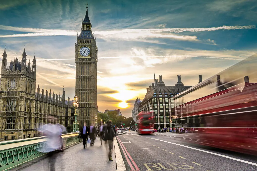 Big Ben and the Houses of Parliament at sunset with motion blur of a red London bus and people walking across Westminster Bridge