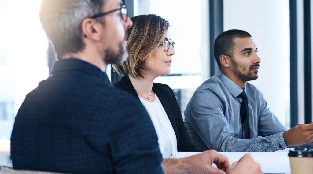 Two business men and a business woman sat in a meeting looking at a presentation