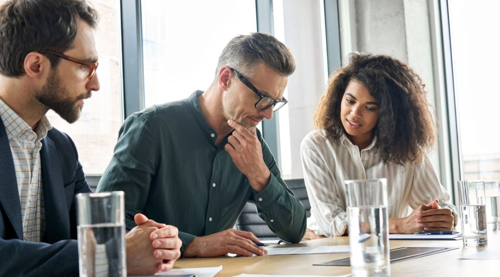 Man viewing paperwork about express clauses with lady and man sat at boardroom table