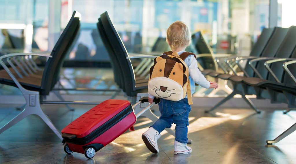 Small boy with tiger rucksack pulling suitcase through airport lounge